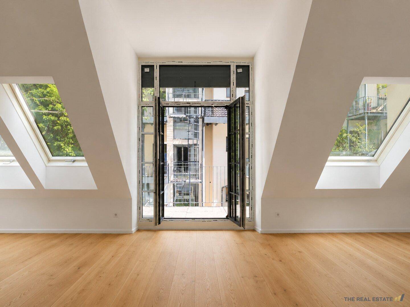 Heller Dachbodenraum mit Holzboden, schrägen Wänden und einem französischen Balkon mit Blick nach draußen.