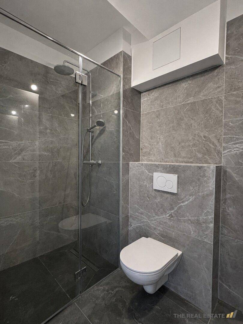 Modernes Badezimmer mit grauen Fliesen, ebenerdiger Dusche und wandhängendem WC.