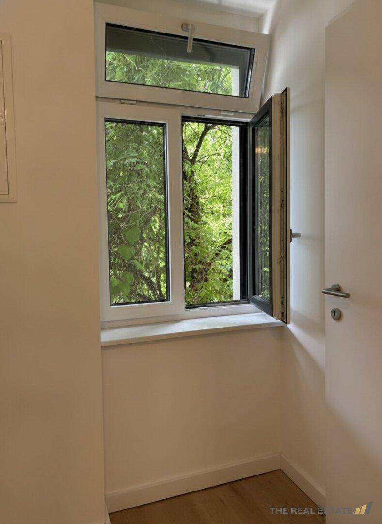 Kleiner Raum mit Fenster und Blick auf grüne Bäume.