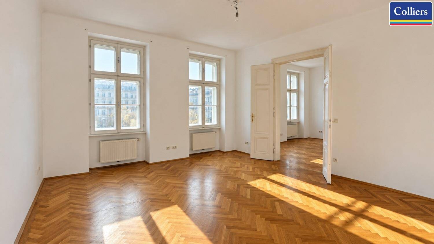 Geräumiges Wohnzimmer mit klassischem Fischgrätparkett und hohen Fenstern, die den Raum erhellen.