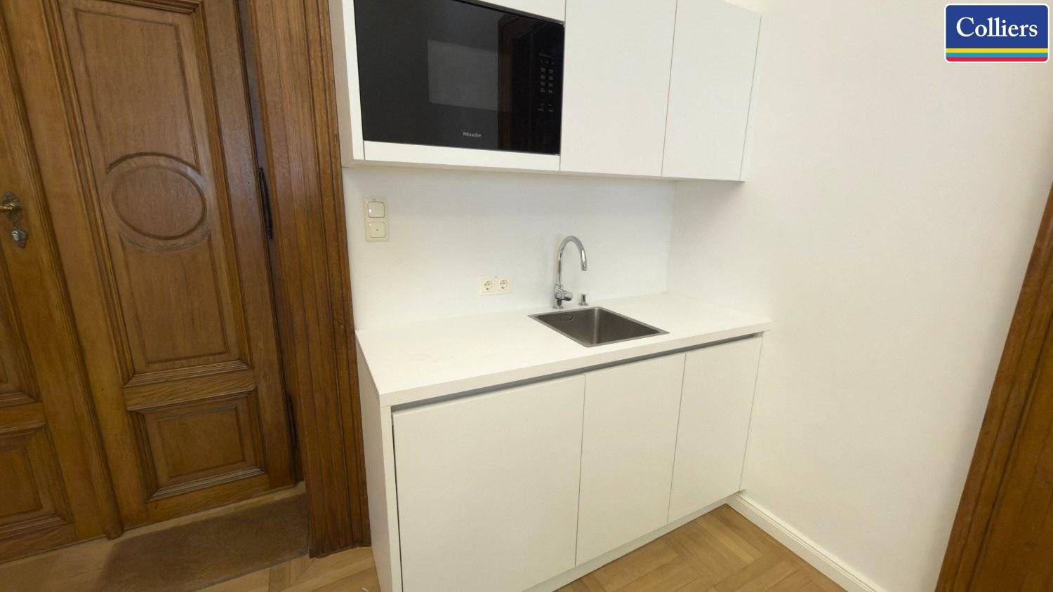 Moderne Küchenzeile mit weißen Schränken, Spüle und integrierter Mikrowelle, ideal für kleine Räume.