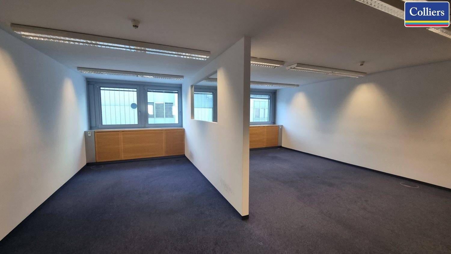Helles Büro mit Teppichboden, großen Fenstern und einer Trennwand für flexible Nutzung.
