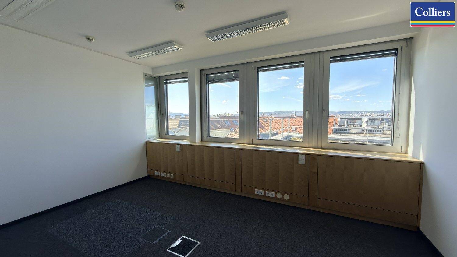 Geräumiges Büro mit Teppichboden, breiter Fensterfront und Blick auf die umliegende Stadt.