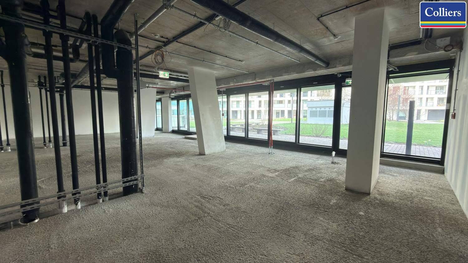 Weitläufiger Gewerberaum im Rohbau mit freiliegenden Rohren und viel Tageslicht durch die Fensterfront.
