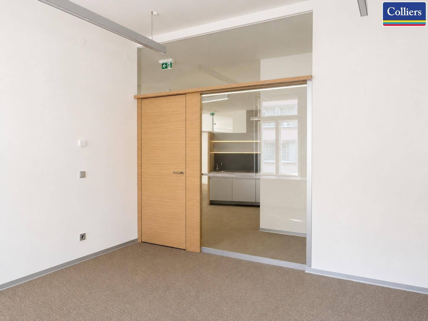 Moderner Bürobereich mit Holztür und Glaswand, die zu einer funktionalen Teeküche führt.
