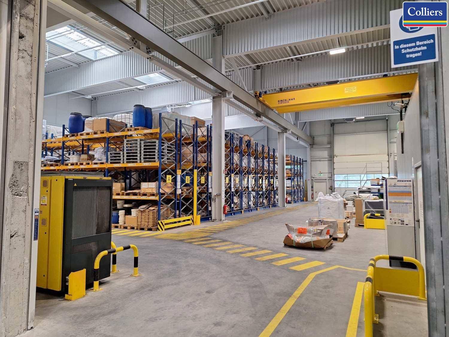 Geräumige Lagerhalle mit hohen Regalen, einem gelben Kran und markierten Bodenbereichen.