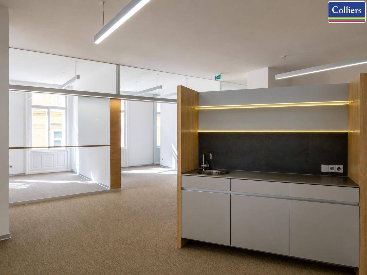 Moderne Teeküche mit Spüle, Unterschränken und beleuchteten Regalen in einem offenen Bürobereich.