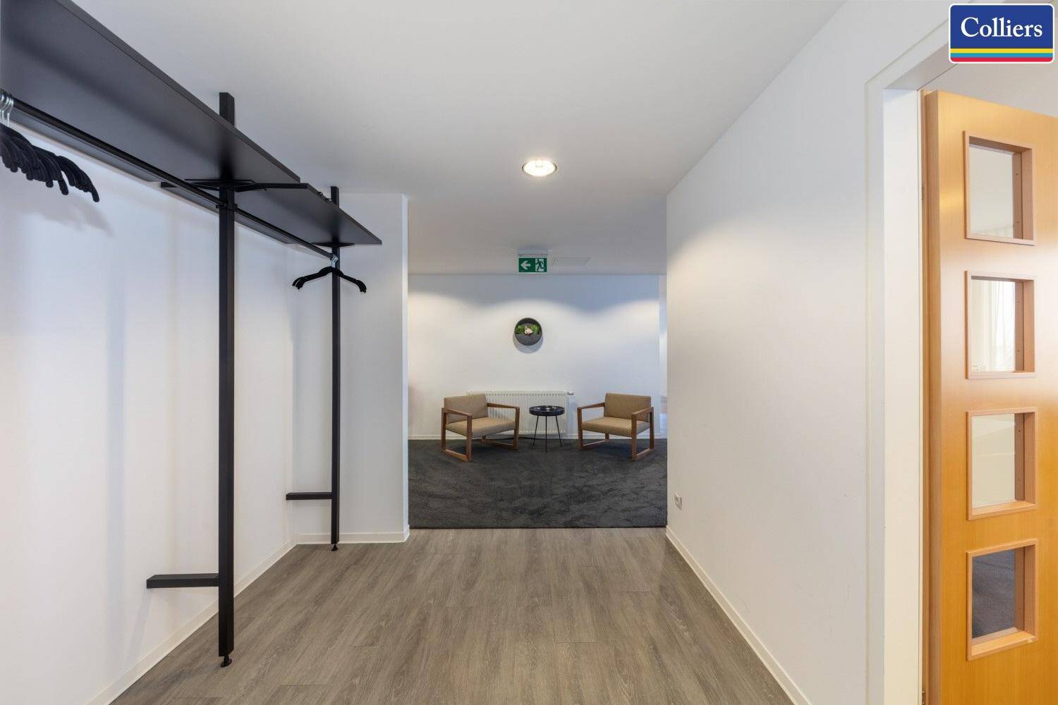 Heller Flur mit Garderobe und Blick auf einen Wartebereich mit Sesseln und Teppichboden.