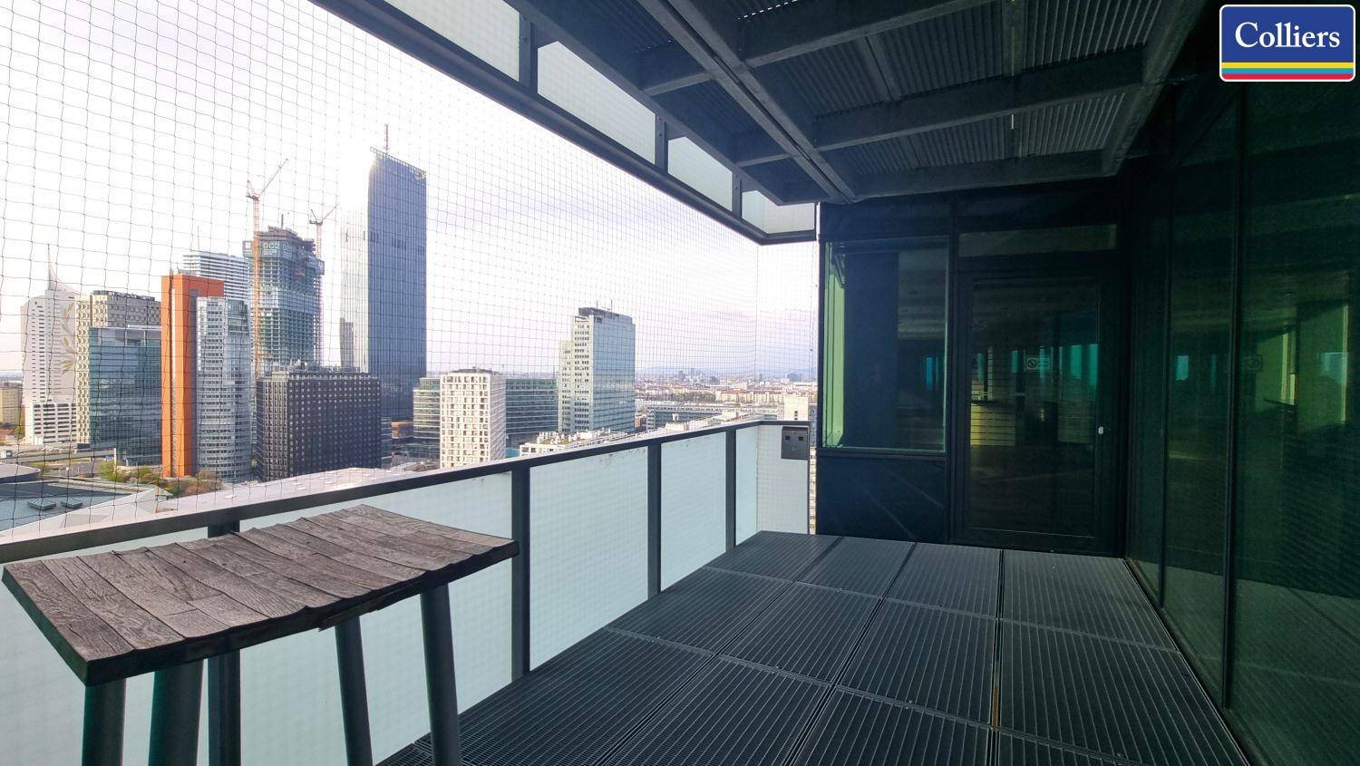 Balkon mit Holztisch und Gitterboden, bietet einen beeindruckenden Blick auf die Stadt und Hochhäuser.