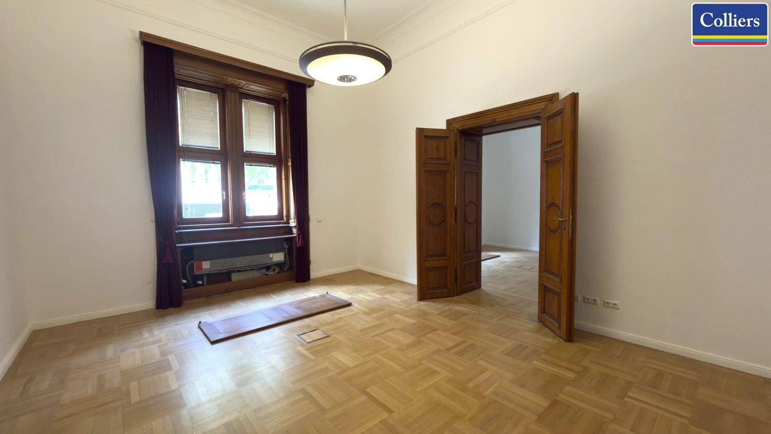 Heller Wohnbereich mit klassischem Parkettboden und hohen Flügeltüren, die zu weiteren Räumen führen.