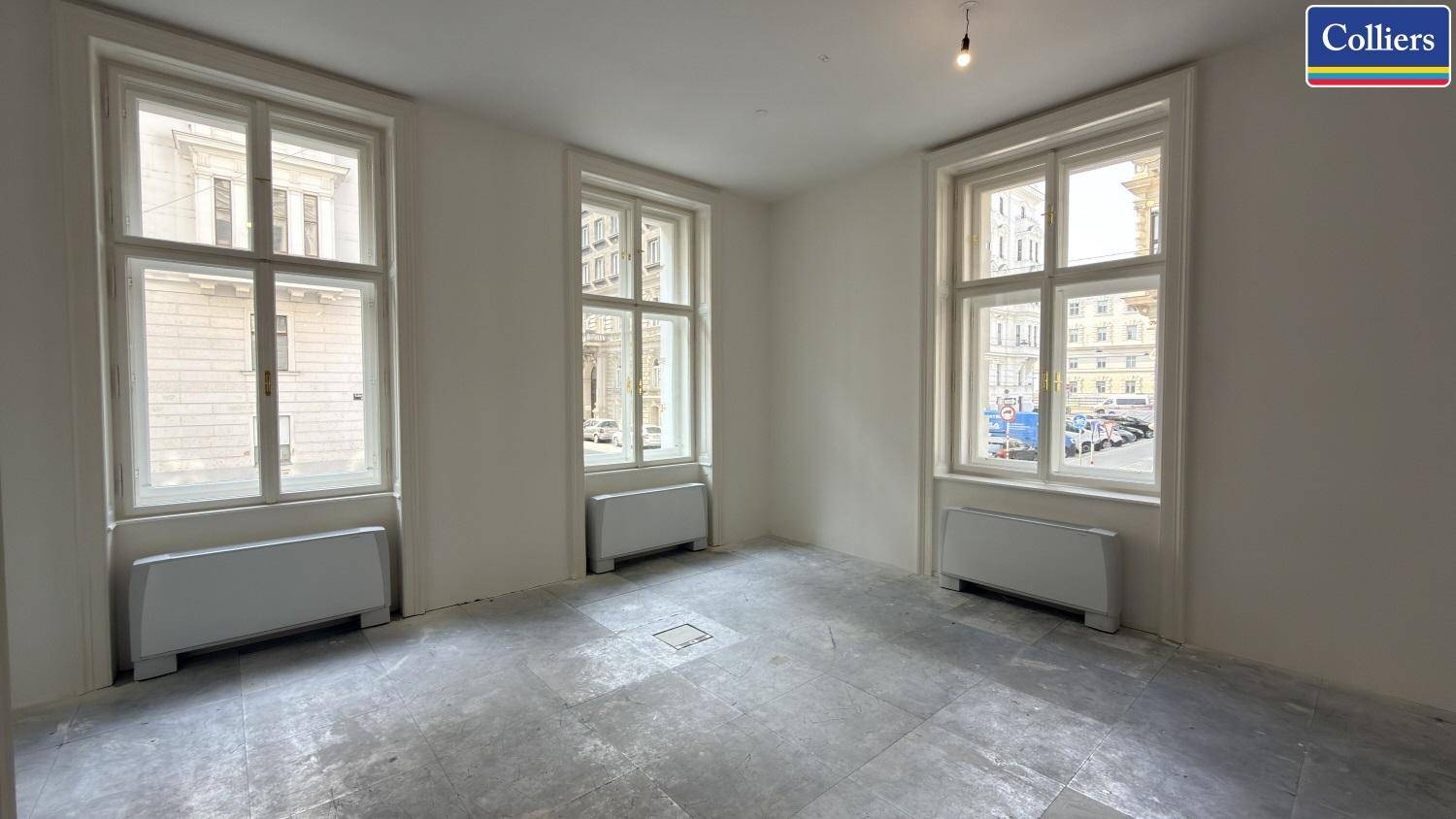 Eckbüro mit drei hohen Fenstern, die eine helle und offene Arbeitsatmosphäre schaffen, und einem Steinboden.