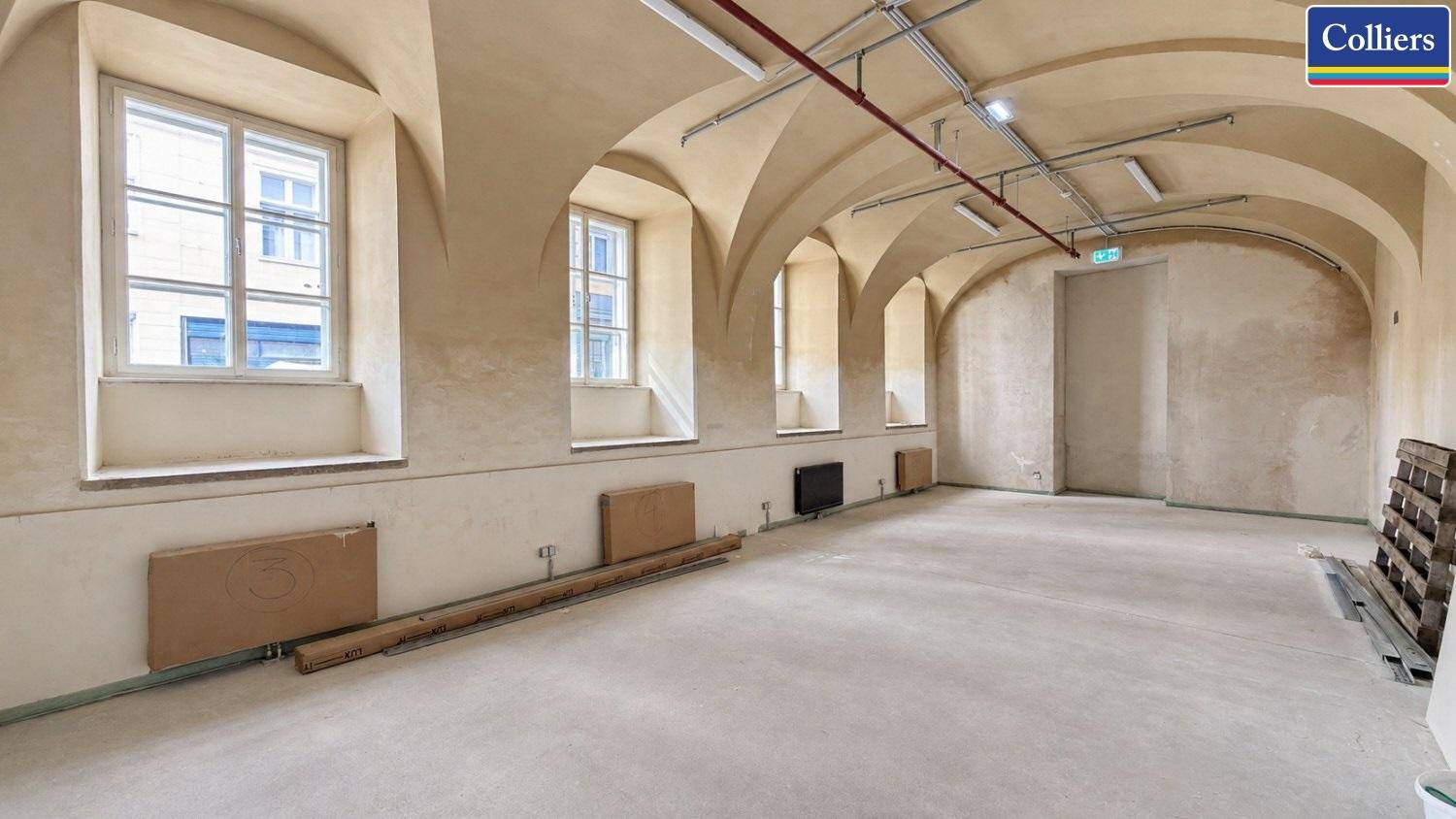 Großer, leerer Raum mit Gewölbedecken, vielen Fenstern und einem Betonboden, bereit für den Ausbau.