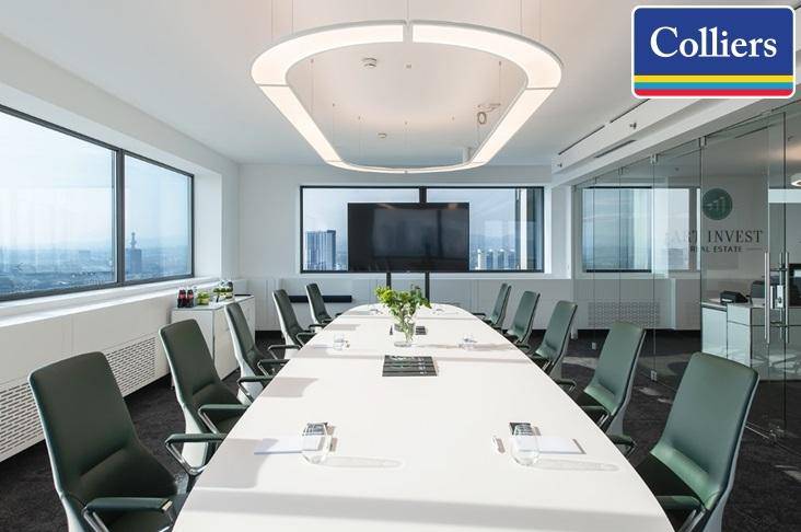 Moderner Konferenzraum mit langem Tisch, bequemen Stühlen und großem Bildschirm mit Stadtblick.