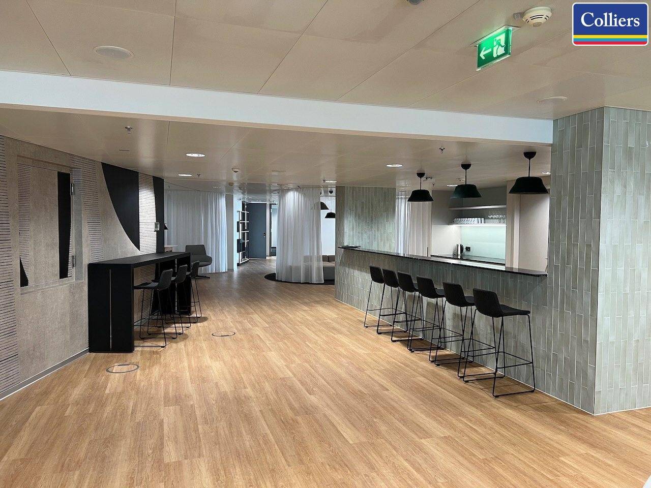 Stilvolle Bar mit Holzboden, modernen Barhockern und einer gefliesten Wand in einem offenen Raum.
