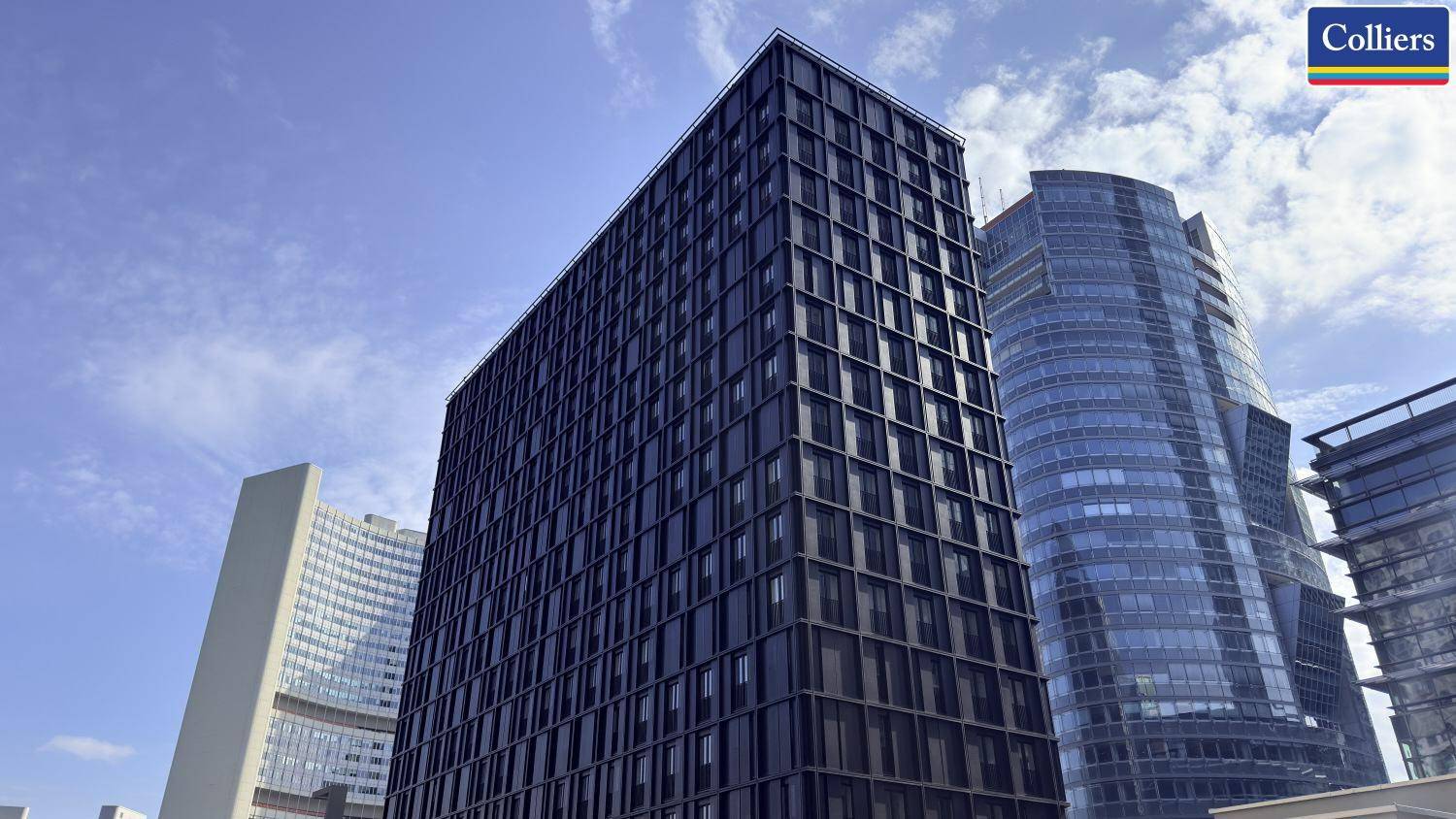 Beeindruckende Ansicht eines hohen, modernen Gebäudes mit dunkler Fassade und vielen Fenstern unter blauem Himmel.
