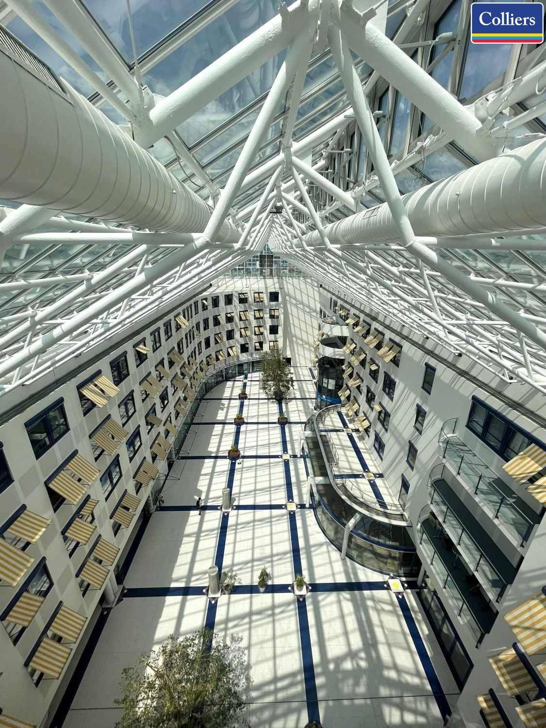 Heller, moderner Atrium-Bereich mit Glasdach, weißen Stahlträgern und mehreren Etagen.