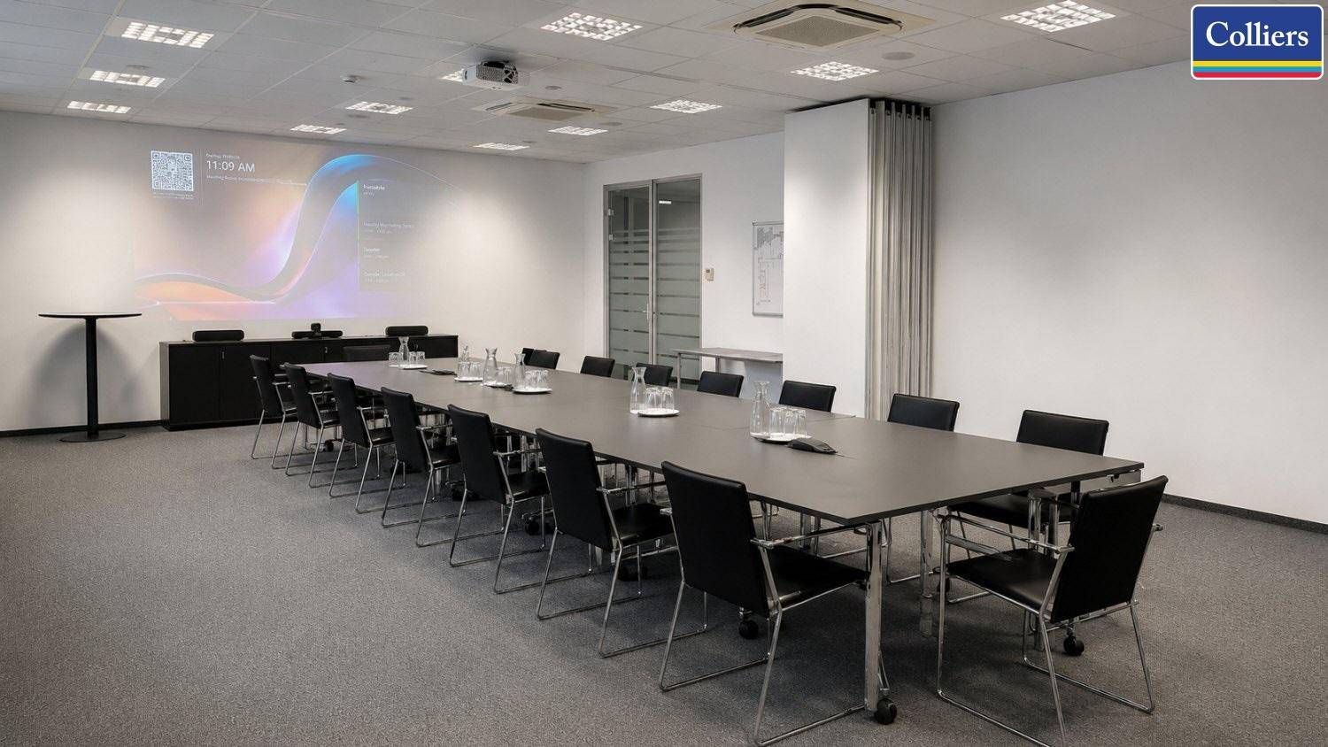 Großer Konferenzraum mit Projektor, langem Tisch und vielen Stühlen, geeignet für umfangreiche Präsentationen und Meetings.