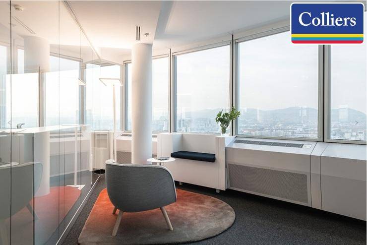 Gemütliche Büroecke mit Sitzgelegenheiten und großen Fenstern mit Blick auf die Stadt.