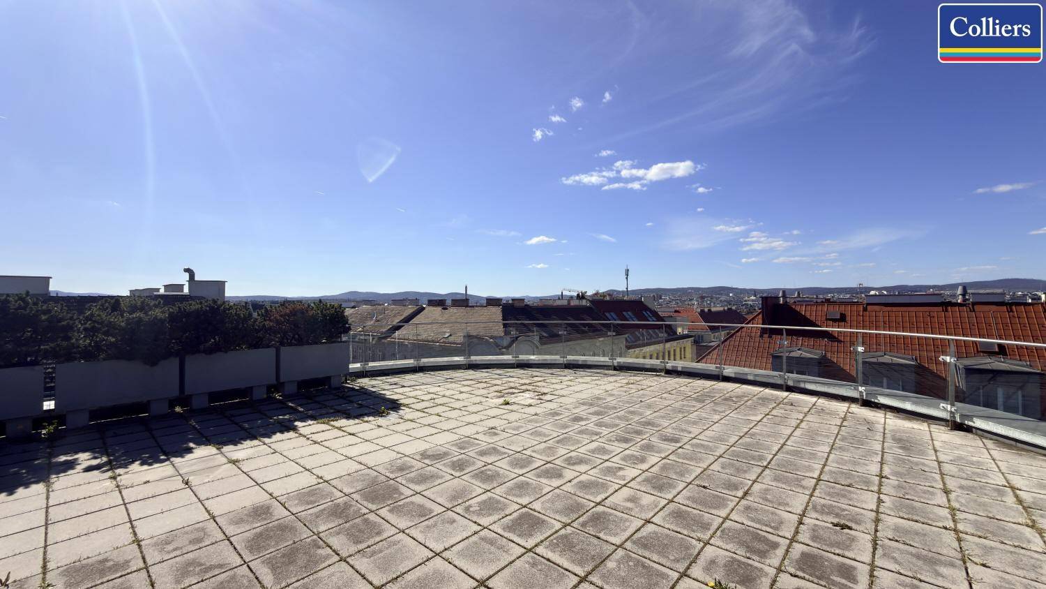 Weitläufige Dachterrasse mit Steinplatten und Panoramablick über die Stadt unter strahlend blauem Himmel.