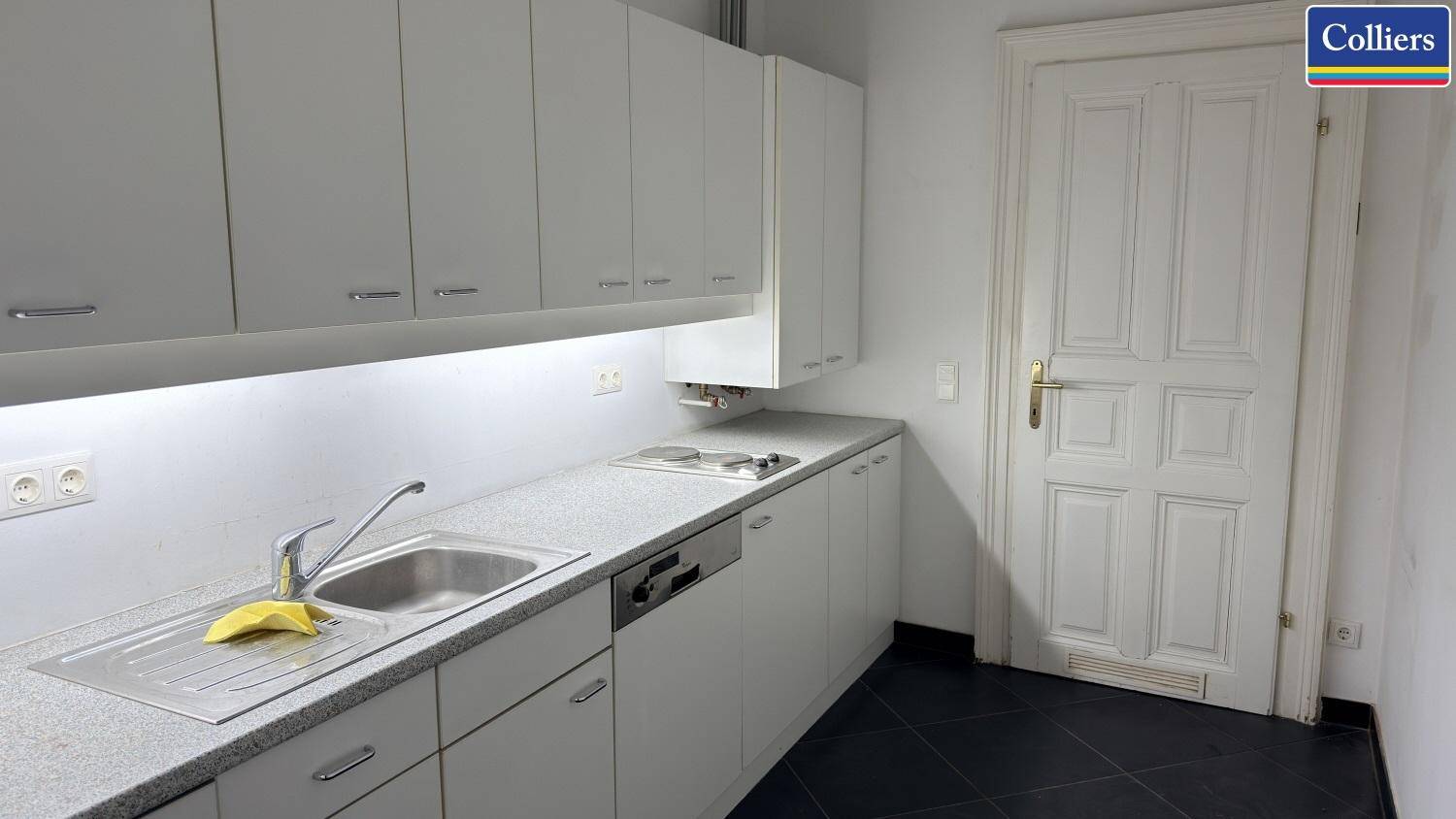 Funktionale Küchenzeile mit weißen Schränken, Spüle und Kochfeld, ideal für eine kleine Büroküche.