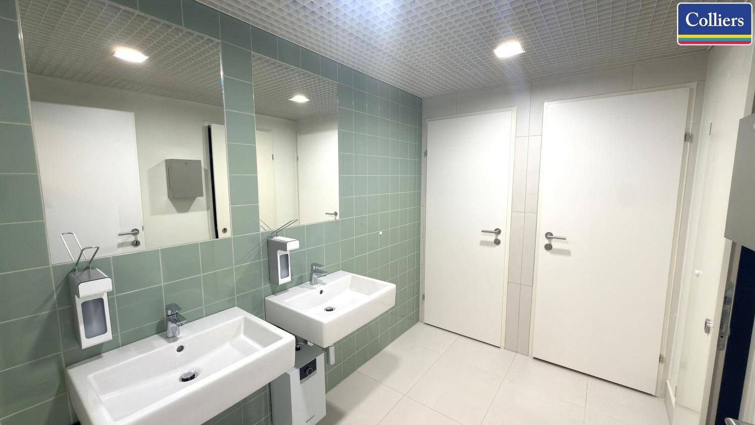 Helles Badezimmer mit zwei modernen Waschbecken und großen Spiegeln, gefliest in hellem Grün und Weiß.