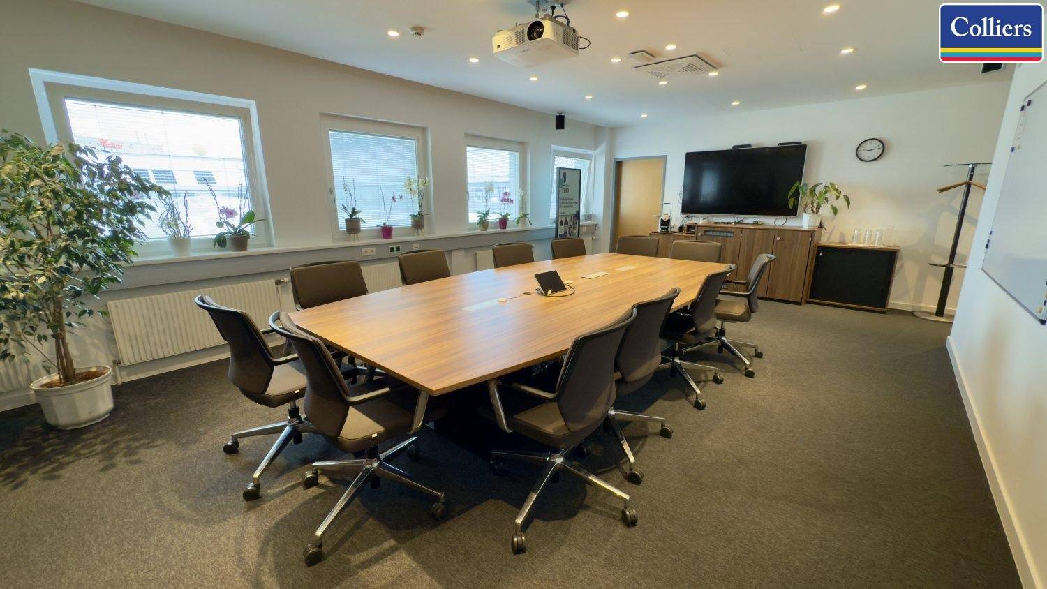 Großer Konferenzraum mit langem Holztisch, bequemen Stühlen und einem Beamer für Präsentationen.