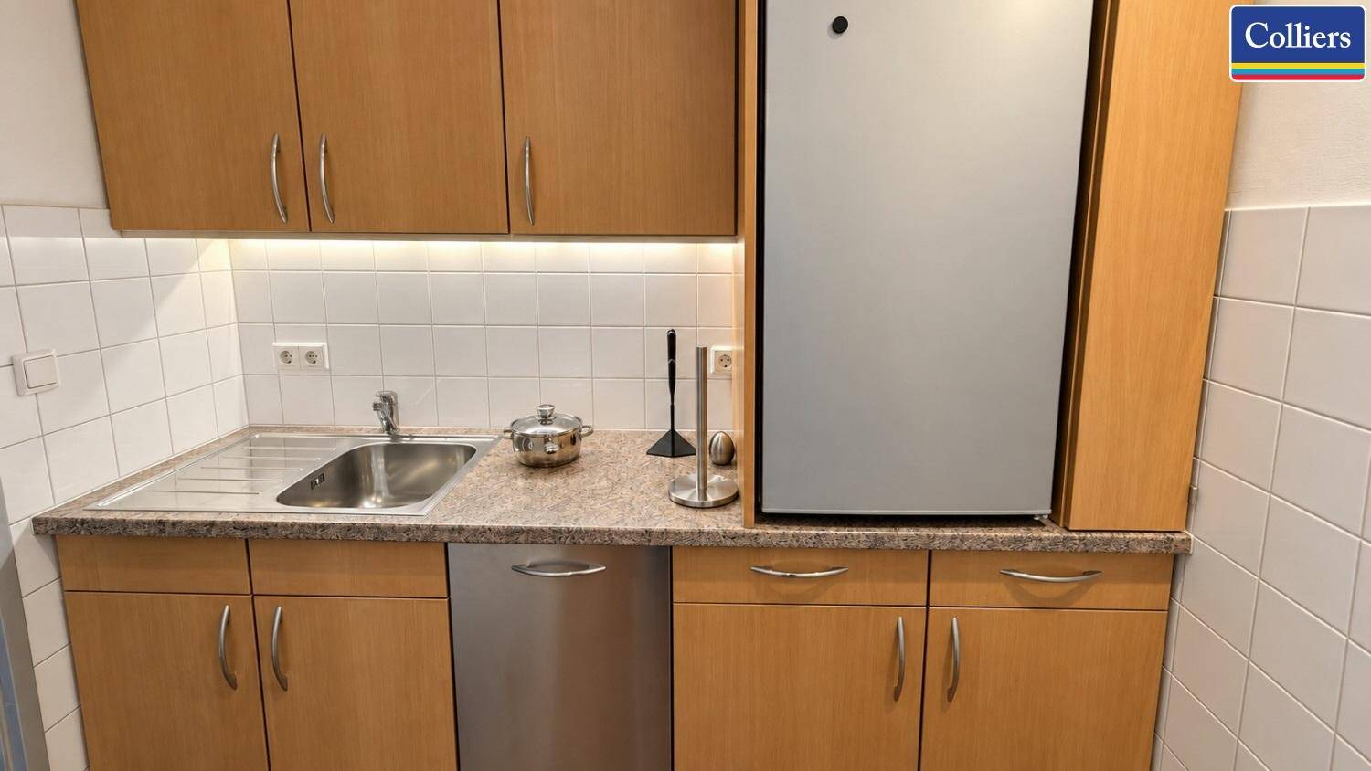 Funktionale Küche mit Holzschränken, Fliesenrückwand und integriertem Kühlschrank.