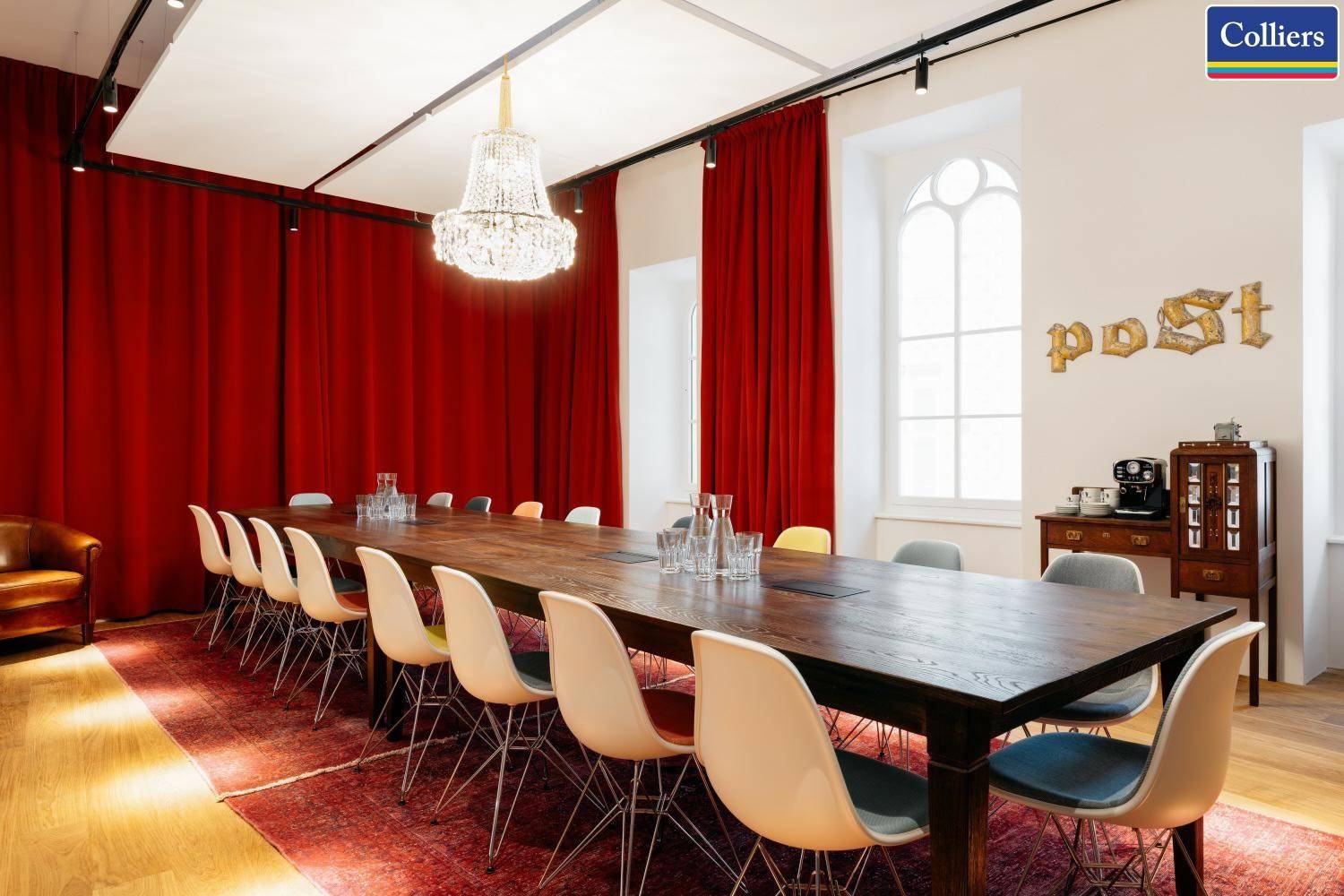 Heller Konferenzraum mit großem Holztisch, modernen Stühlen und einem eleganten Kronleuchter.