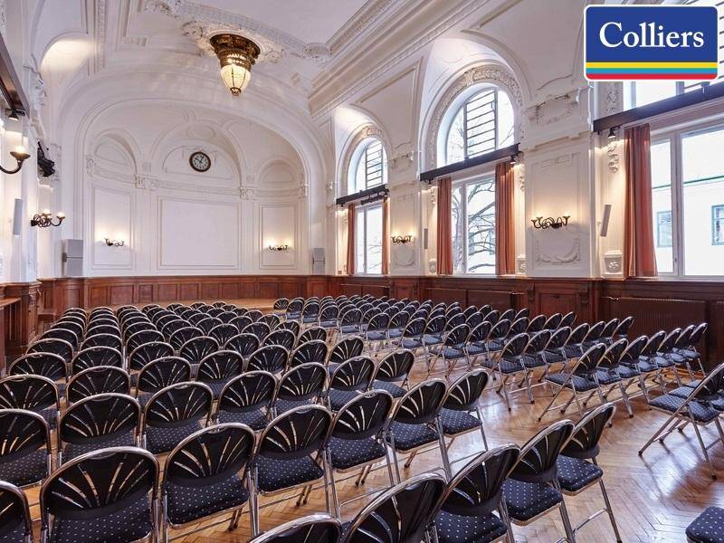 Großer Konferenzsaal mit vielen Stühlen, hohen Fenstern und klassischer Deckenverzierung für Veranstaltungen.