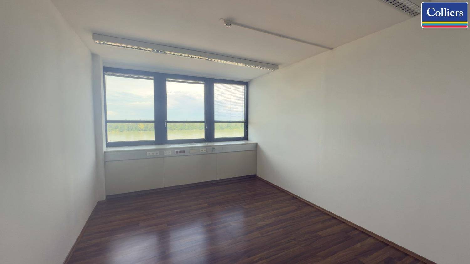 Leeres Büro mit Holzboden und einer Fensterfront, die einen weiten Blick auf die Umgebung bietet.
