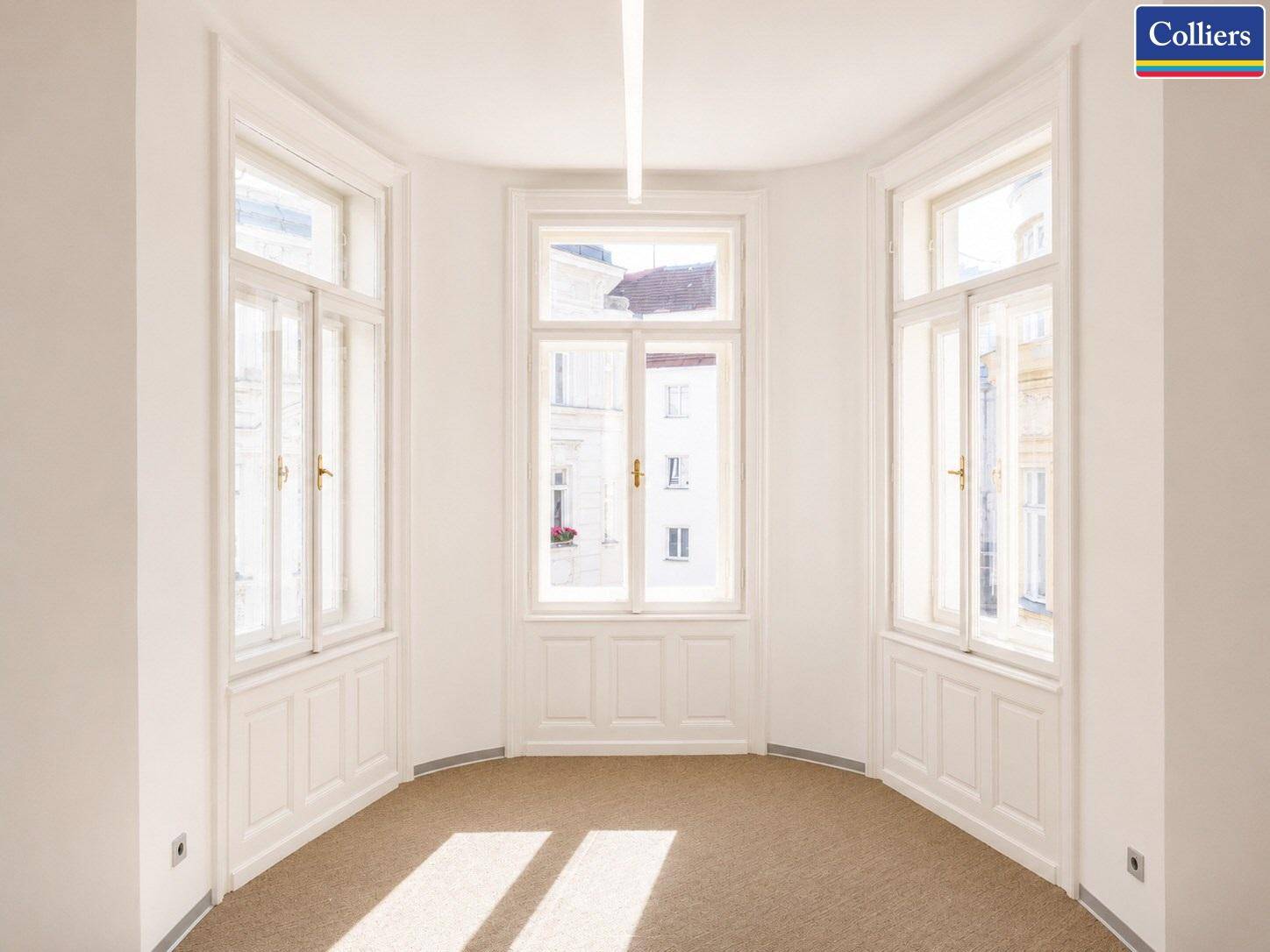 Eckbüro mit drei großen Fenstern, die viel natürliches Licht hereinlassen, und hellem Teppichboden.