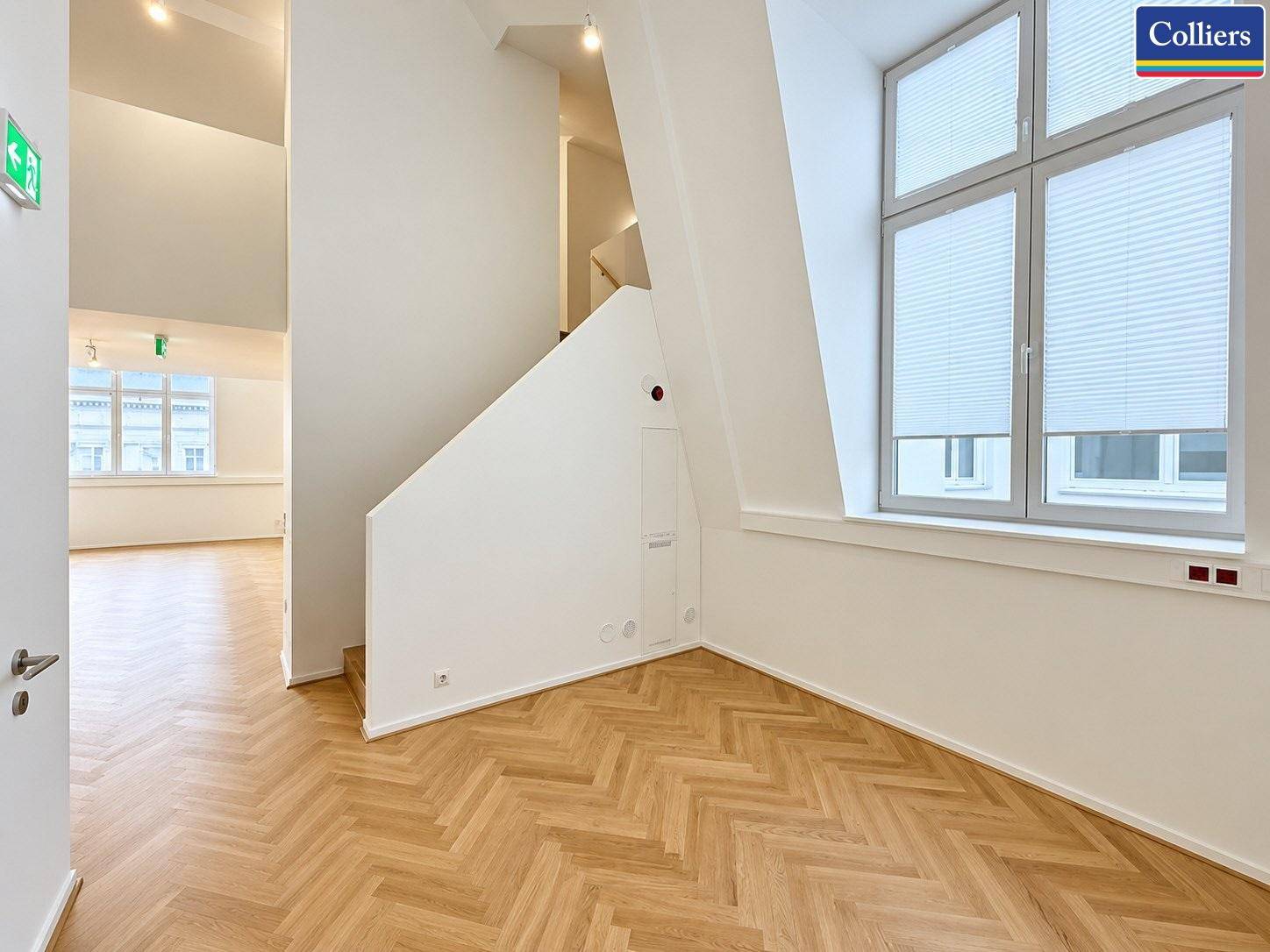 Eingangsbereich eines Büros mit Holztreppe, Fischgrätparkett und Fenster mit Plissees.
