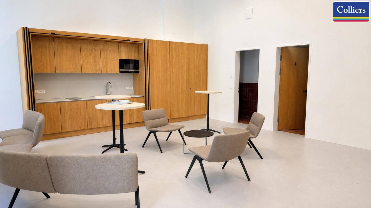 Gemütlicher Loungebereich mit bequemen Sesseln und einer versteckten Küchenzeile in Holzoptik.