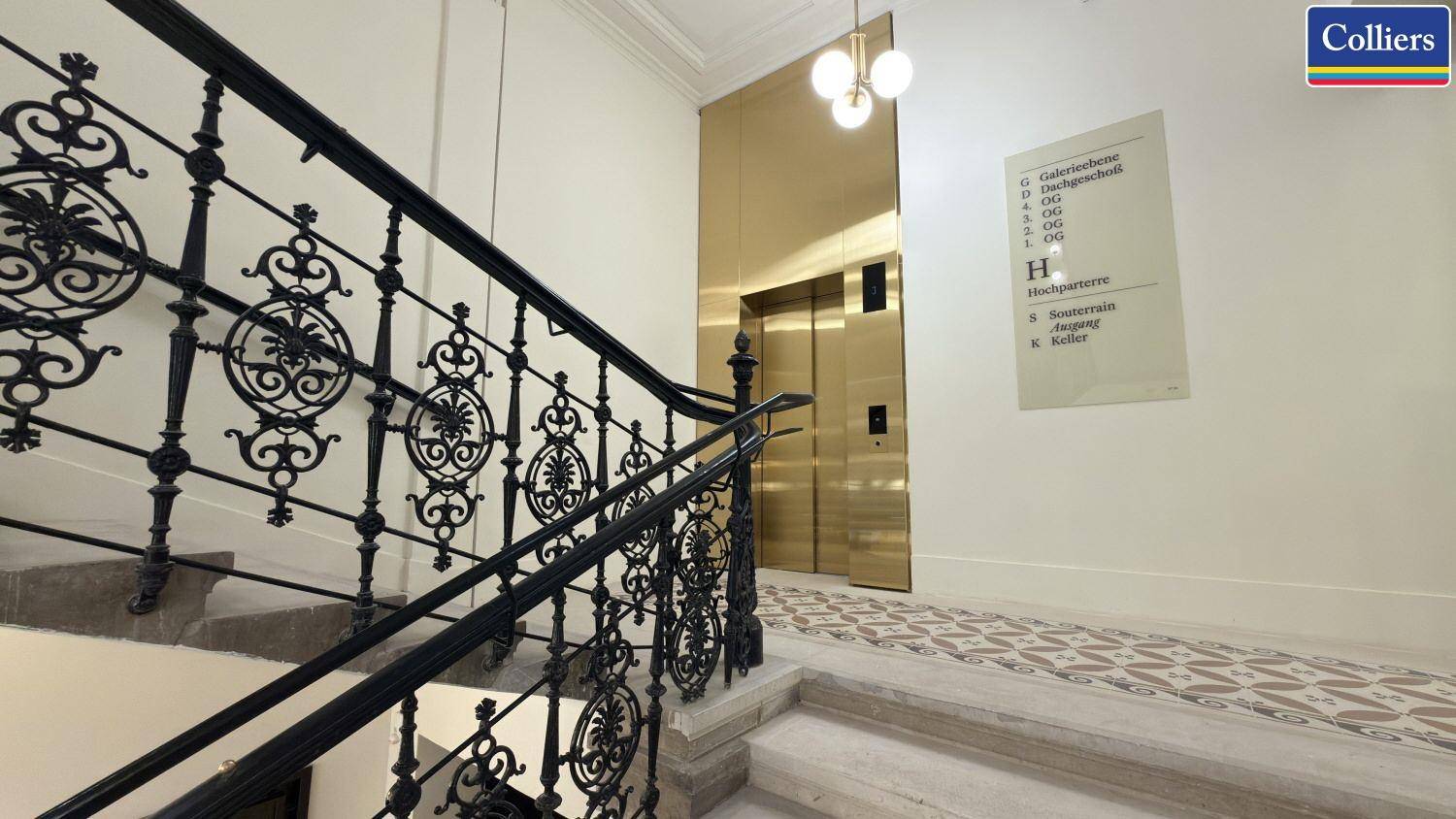 Elegantes Treppenhaus mit schmiedeeisernem Geländer und einem goldenen Aufzug, der den Zugang zu den Etagen ermöglicht.
