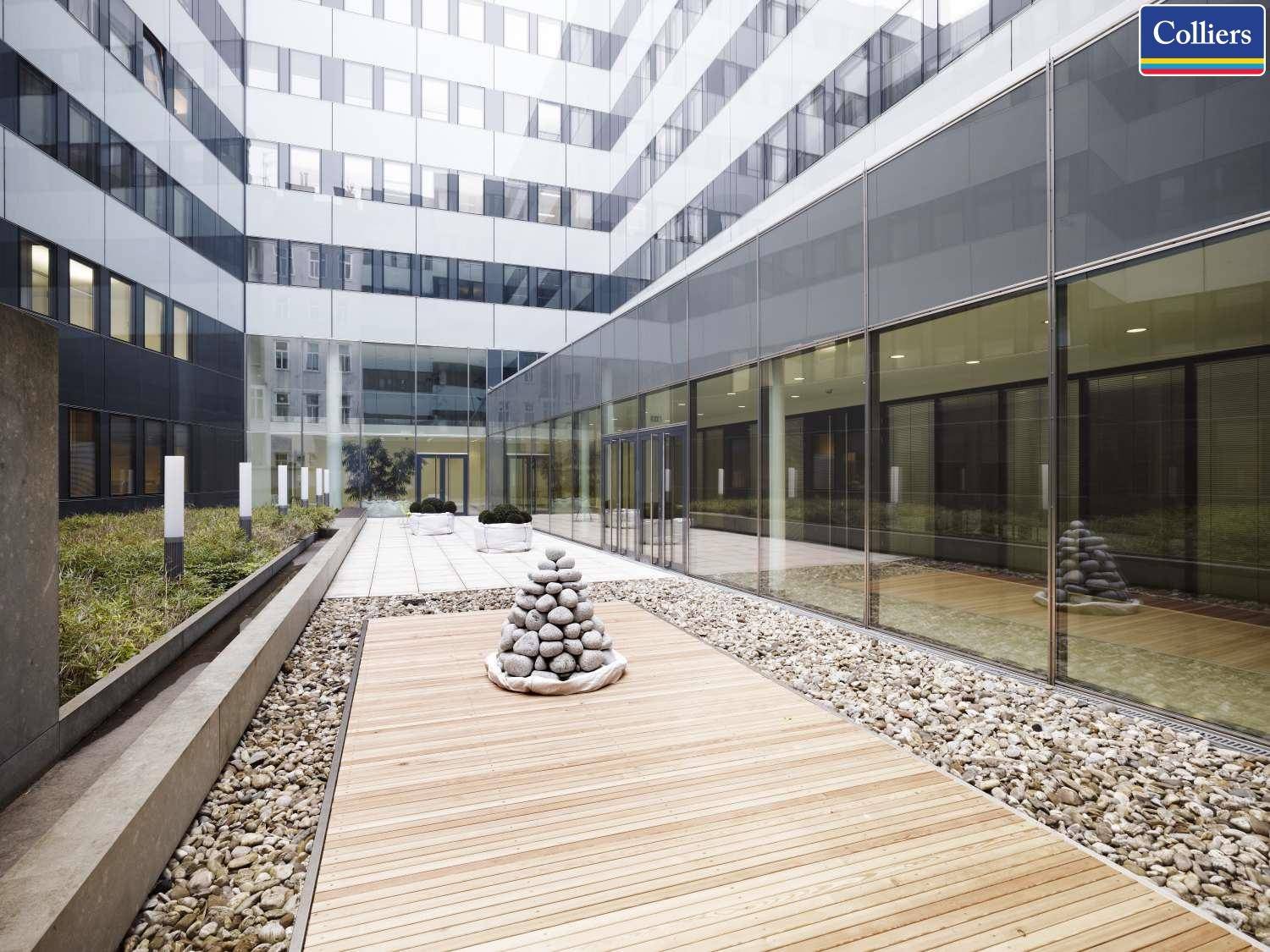 Moderner Innenhof mit Holzdeck, Kiesflächen und minimalistischer Bepflanzung, umgeben von Bürogebäuden.