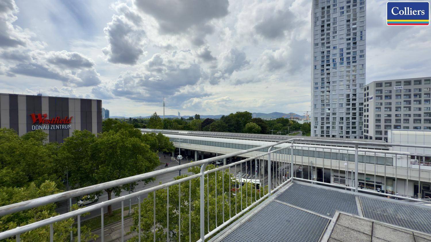 Weitläufige Dachterrasse mit Panoramablick auf die Stadt, moderne Hochhäuser und eine Bahntrasse.