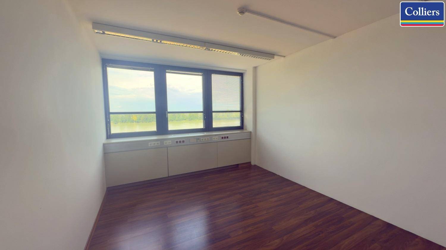 Leeres Büro mit dunklem Holzboden und einer Fensterfront, die einen weiten Blick auf die Landschaft bietet.