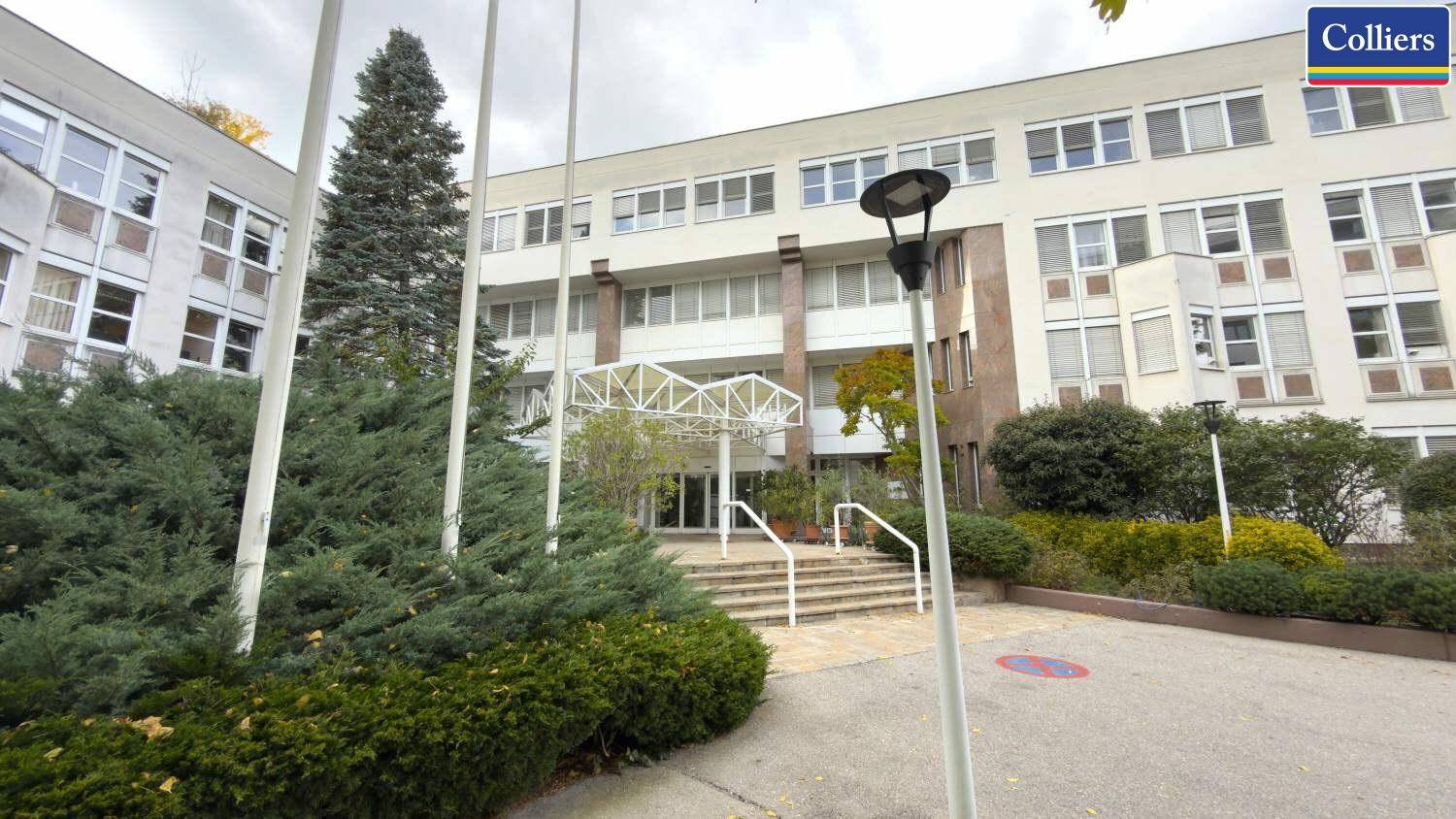Modernes Bürogebäude mit mehreren Etagen, großen Fenstern und einem gepflegten Eingangsbereich mit Treppe.