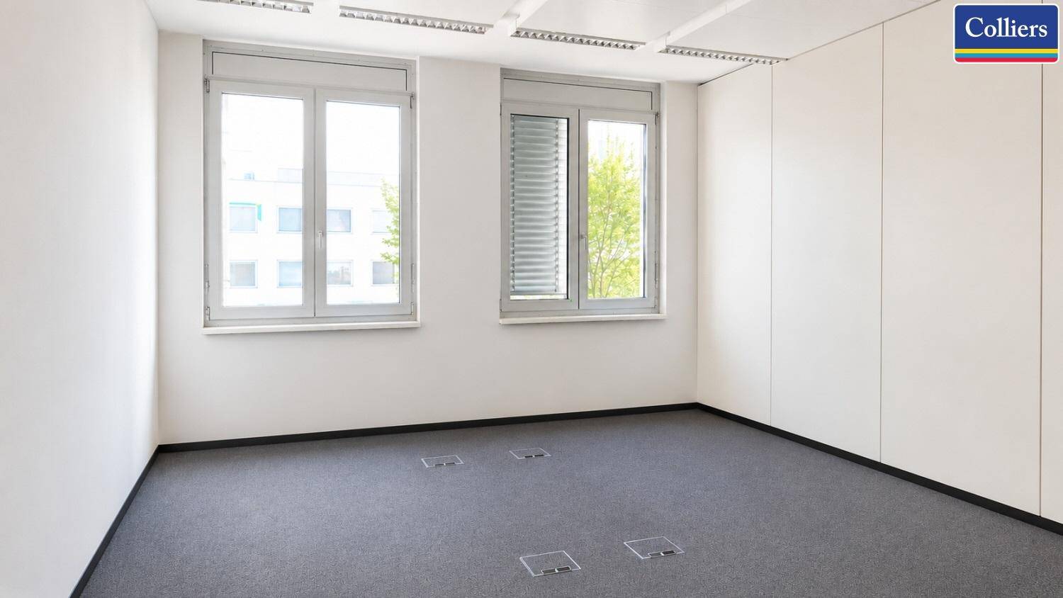 Kleineres, leeres Büro mit zwei Fenstern, Teppichboden und Deckenplatten.