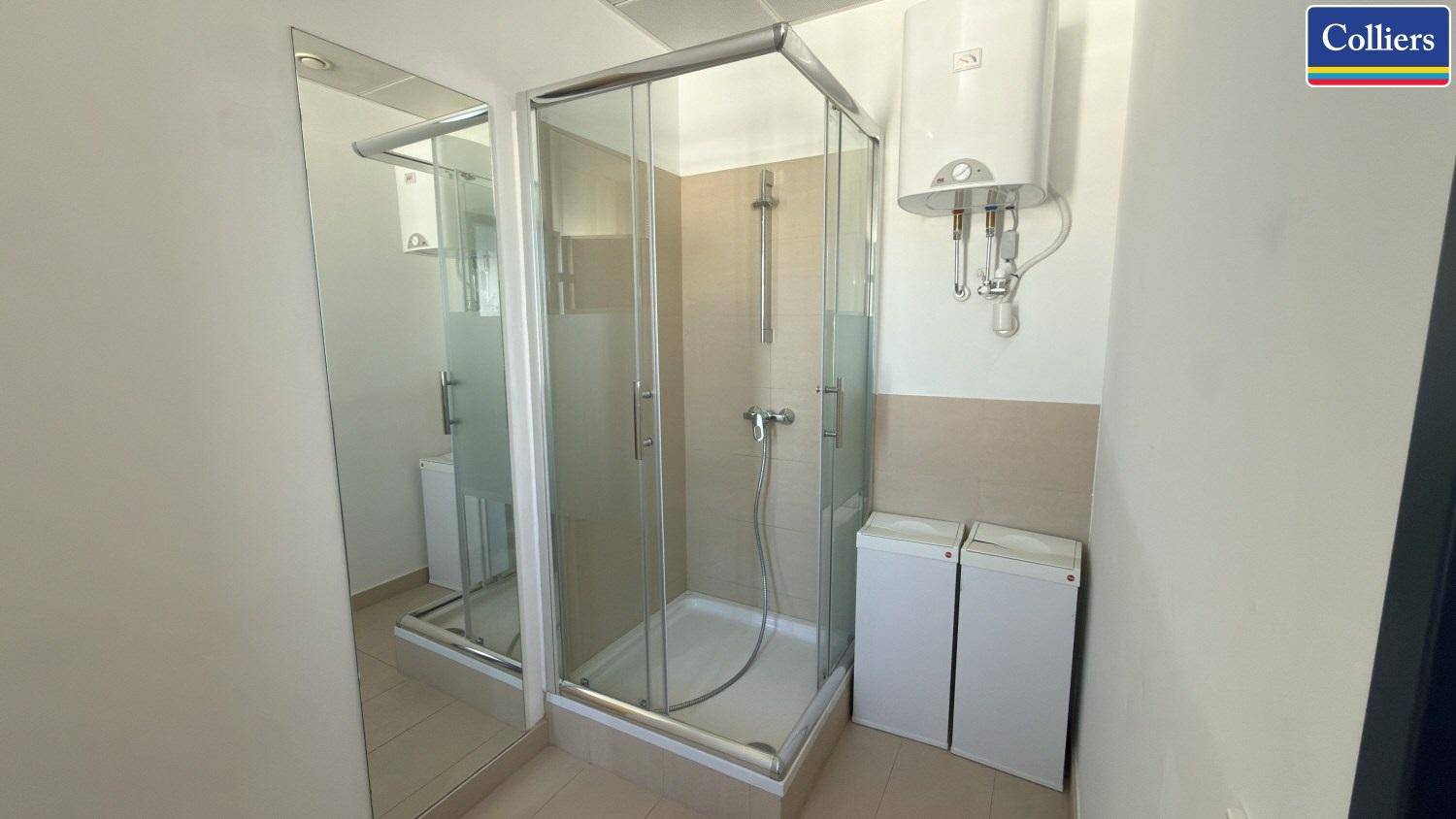 Kleines Badezimmer mit Duschkabine, Boiler und hellem Fliesenboden.