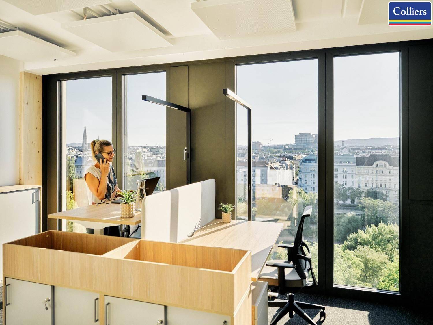 Heller Büroarbeitsplatz mit Schreibtischen, Bürostühlen und weitem Stadtblick durch große Fenster.