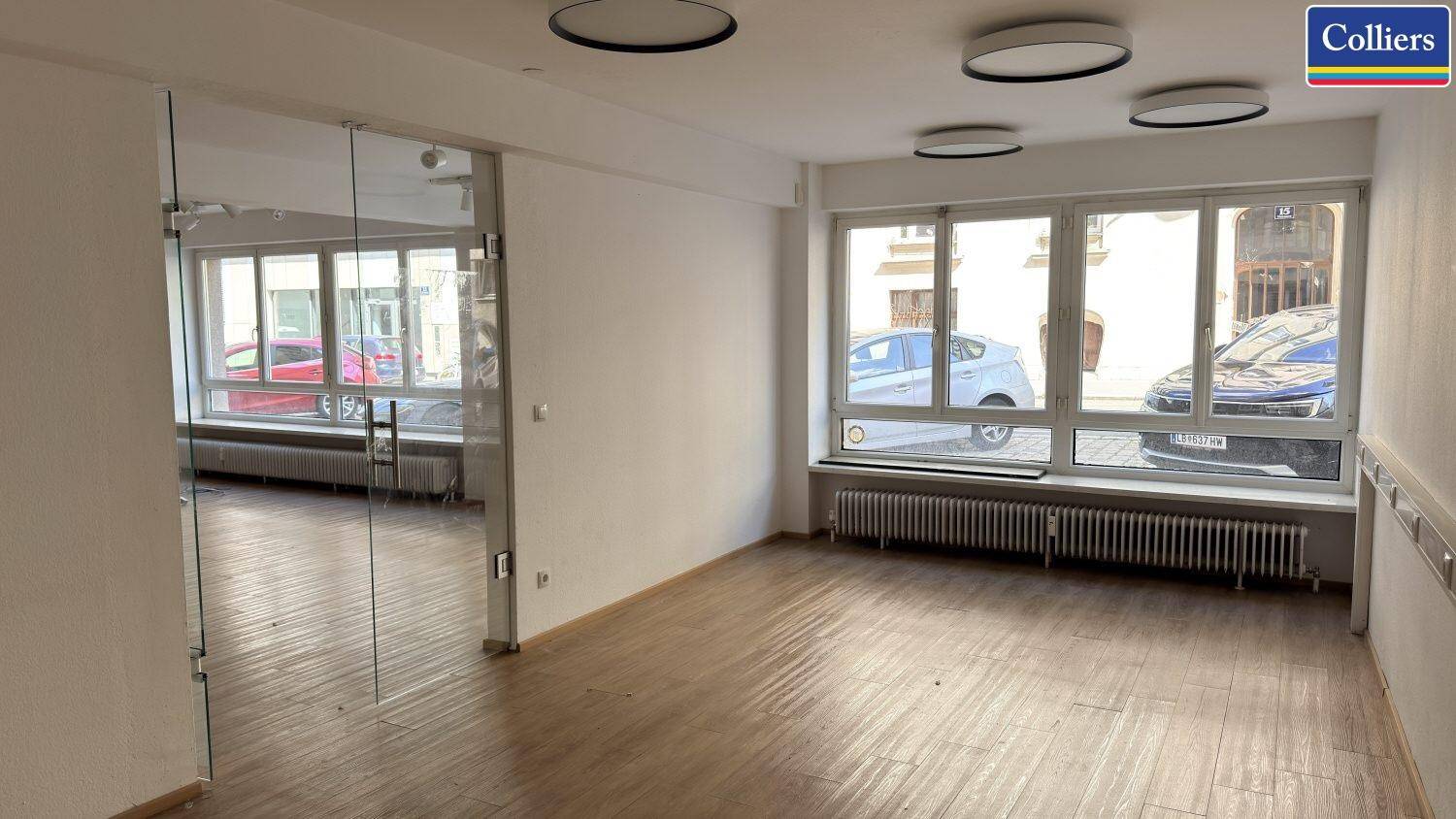 Innenansicht eines Geschäftsraums mit großen Fenstern und einer Glastür, die zu einem weiteren Bereich führt.