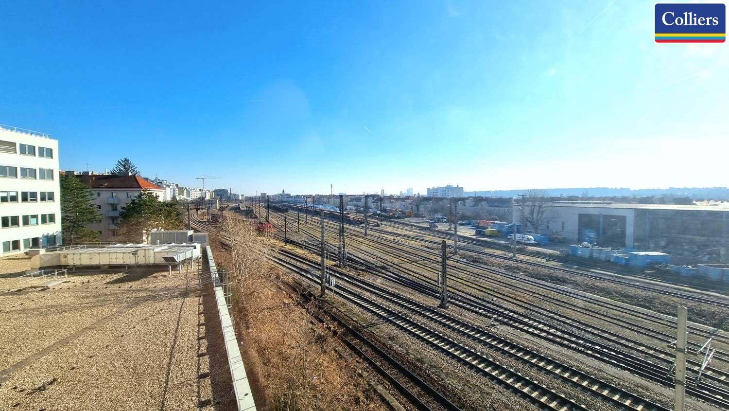 Weitläufiger Blick auf Bahngleise und die städtische Skyline unter einem klaren blauen Himmel.