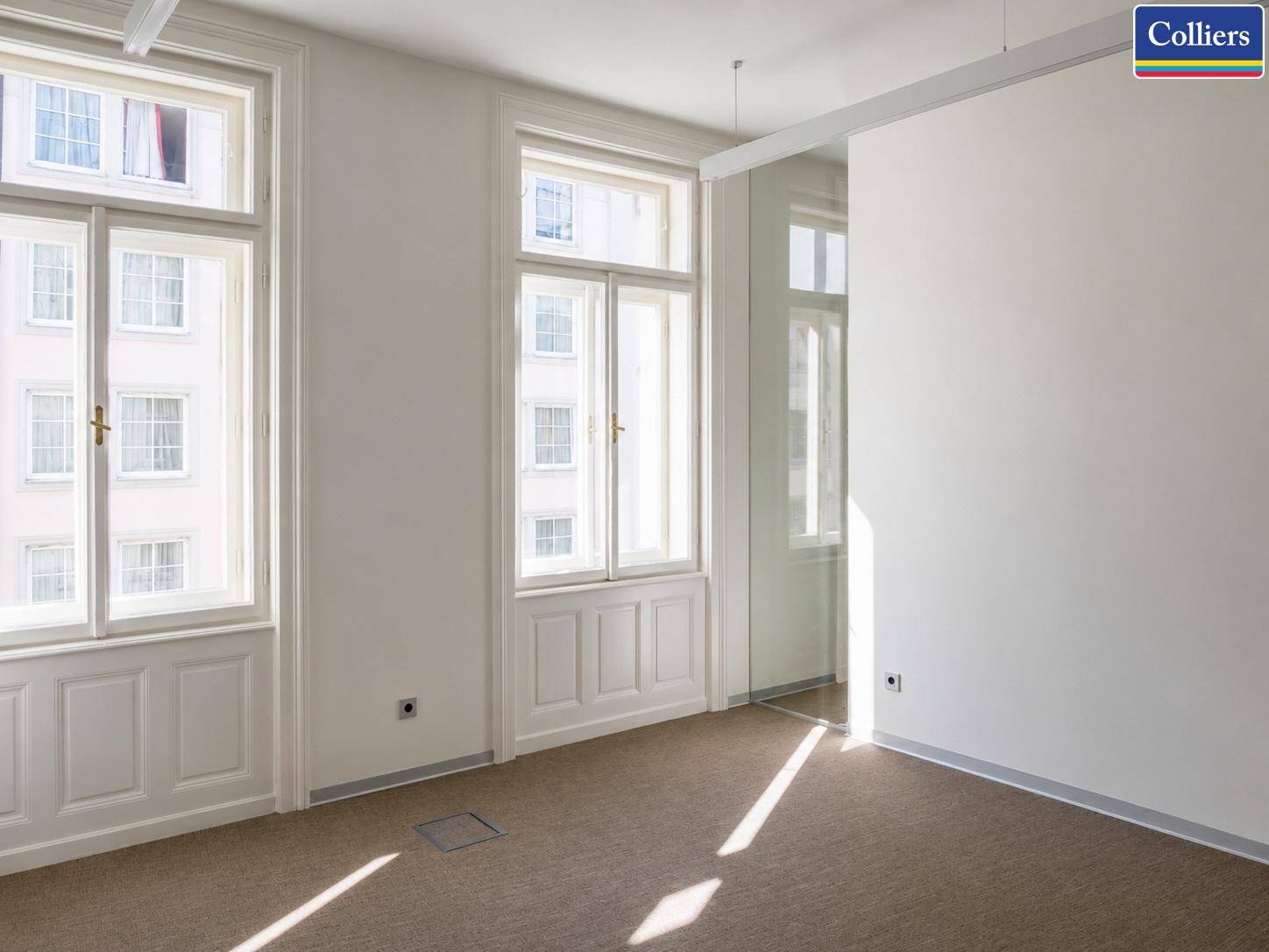 Heller Büroraum mit großen Fenstern, Teppichboden und einer modernen Glaswand für flexible Gestaltung.