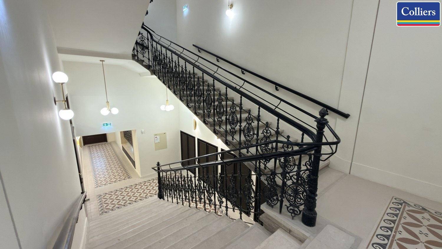 Historisches Treppenhaus mit kunstvollem Geländer und gemusterten Fliesen, das zu den oberen Etagen führt.