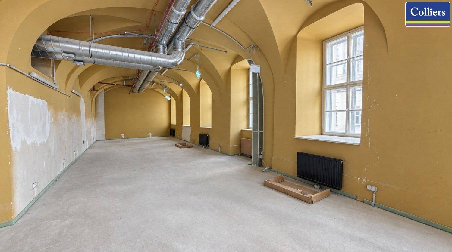 Geräumiger Gewerberaum mit hohen Gewölbedecken, sichtbaren Lüftungsrohren und großen Fenstern.