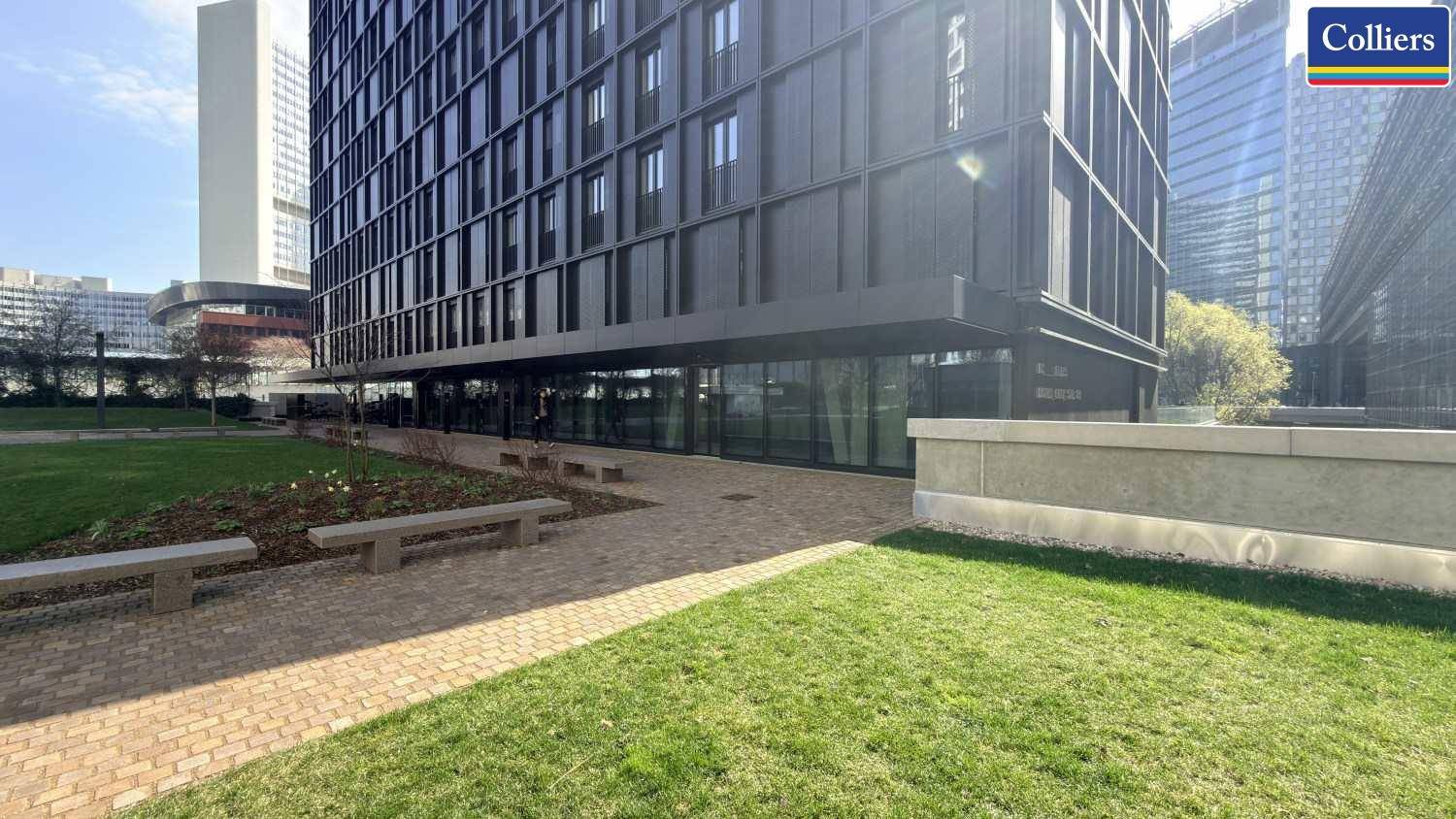 Ansicht eines modernen Geschäftsgebäudes mit dunkler Fassade, umgeben von einer gepflegten Rasenfläche und Gehwegen.