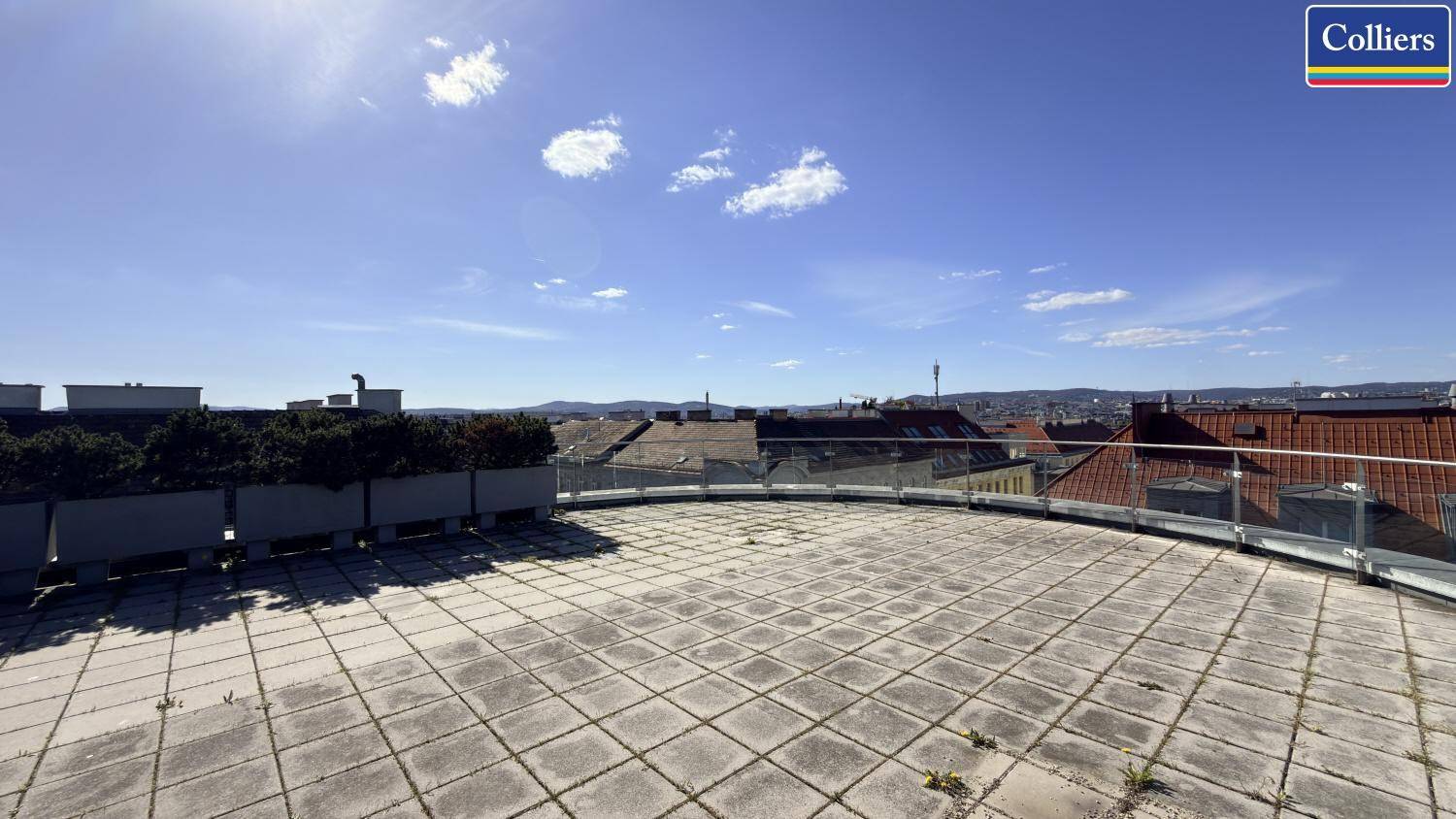 Weitläufige Dachterrasse mit Steinplatten und Panoramablick über die Stadt unter strahlend blauem Himmel.