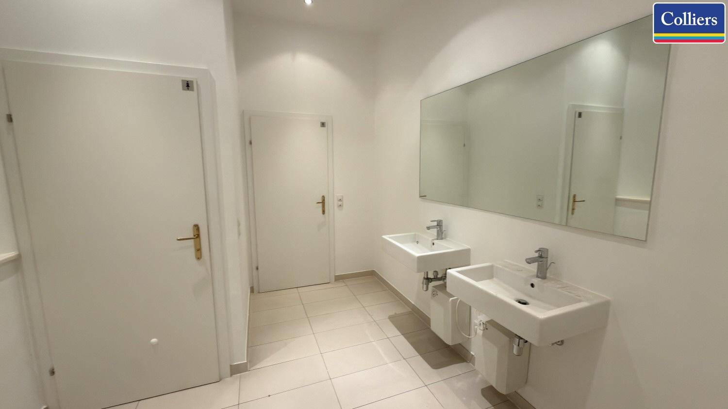 Modernes Badezimmer mit zwei Waschbecken, großem Spiegel und hellen Fliesen, in gutem Zustand.