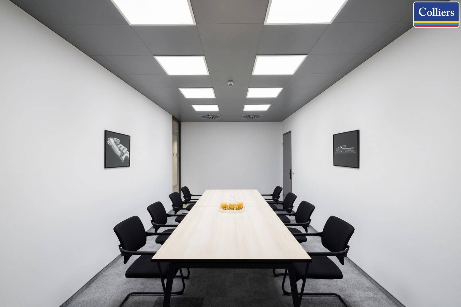 Großer Konferenzraum mit langem Tisch und vielen schwarzen Stühlen, beleuchtet von modernen Deckenleuchten.